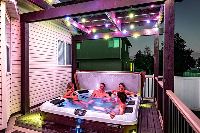 Family in a hot tub under a pergola lit with colorful permanent lights