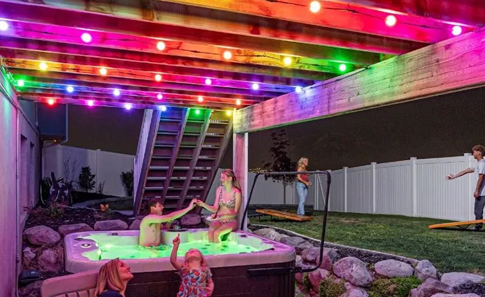Kids playing in a hot tub under a deck lit with rainbow lights