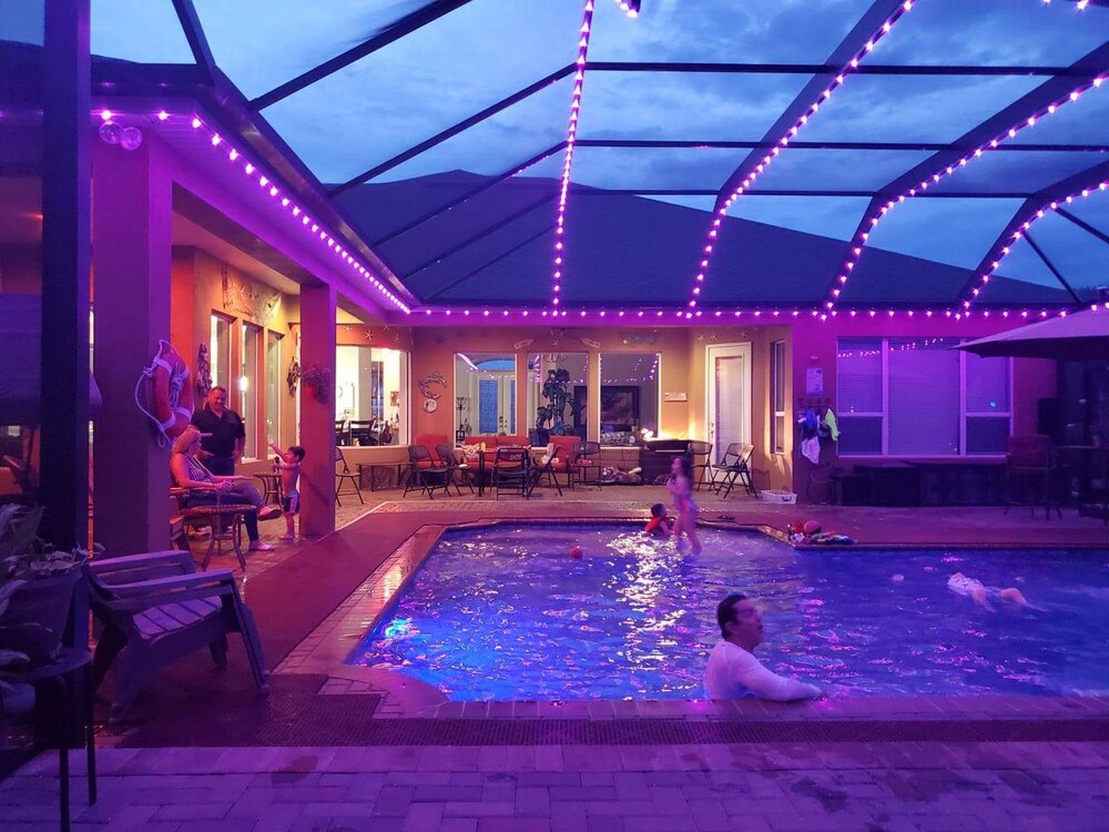 Pool enclosure lit with purple lights while swimmers enjoy the pool