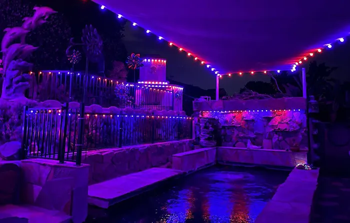 Purple permanent lights around a backyard pool and pergola