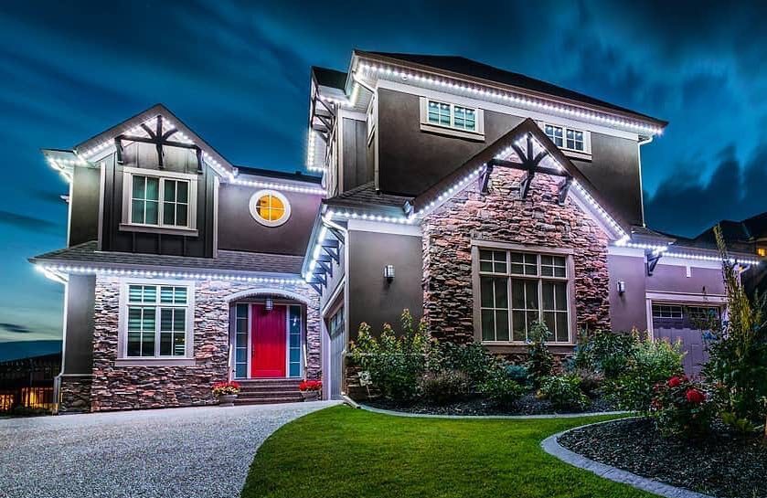 White permanent lights on a stone two-story home at dusk