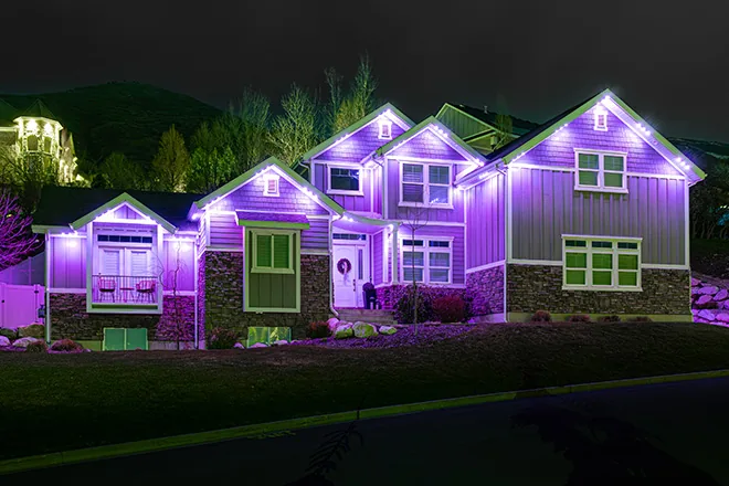 Purple permanent lights on a two-story hillside home